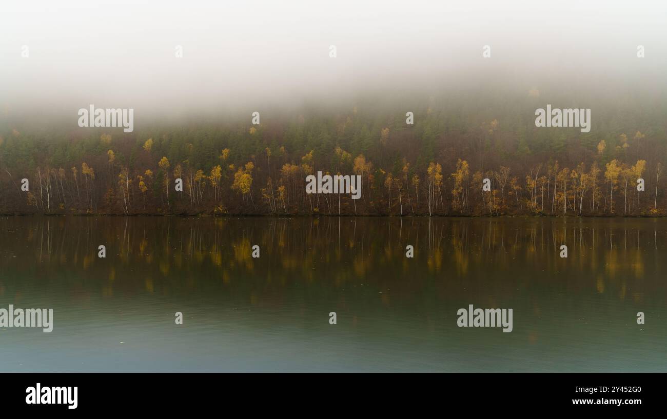 Large fleuve Vag calme des eaux automnales avec des forêts de brumes décidues rouges et jaunes réfléchissantes près de la colonie de Sutovo, République slovaque. Météo Moody et tr Banque D'Images