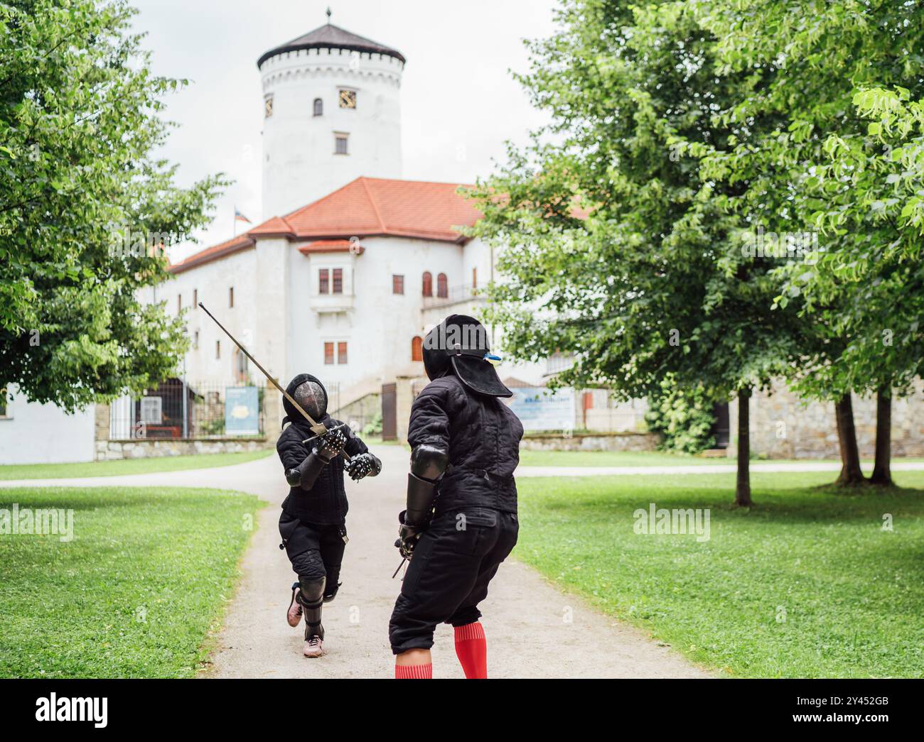 Deux escrimeurs vêtus d'uniformes de protection noirs, des casques avec des masques faciaux sont des clôtures dans le parc de la ville en utilisant de longues épées historiques en métal médiéval, practi Banque D'Images