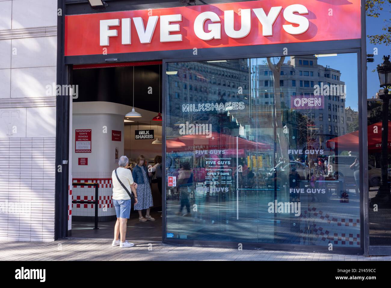 Barcelone, Espagne - 15 septembre 2024 : une scène de la Plaza Cataluña montre des gens entrant dans un cinq gars, la vif vif vif vif vitrine rouge contraste avec BARC Banque D'Images