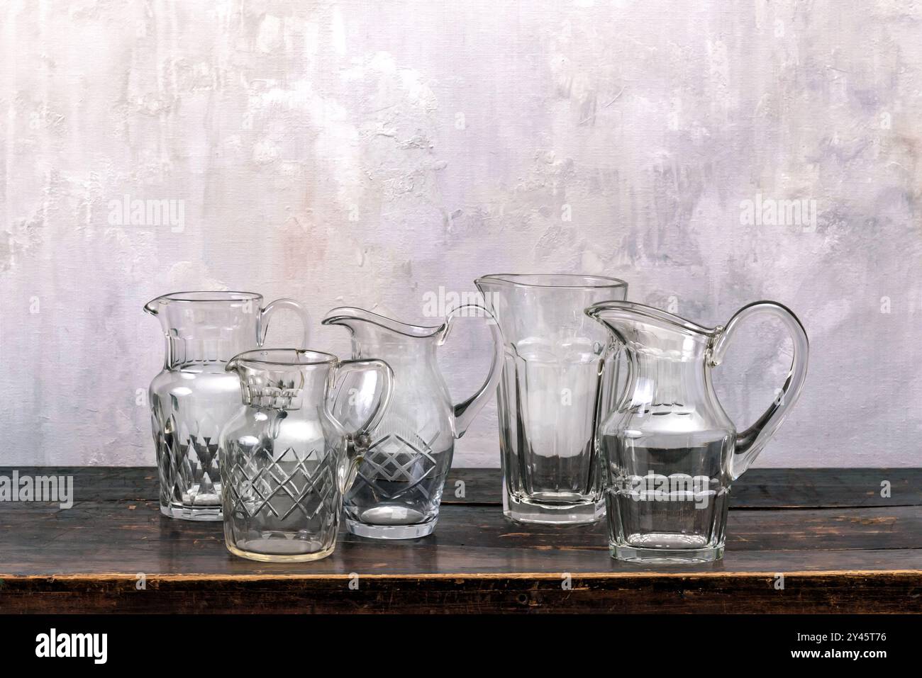 Ensemble de pichets en verre transparent placés sur le dessus de la table en bois contre le mur gris minable Banque D'Images