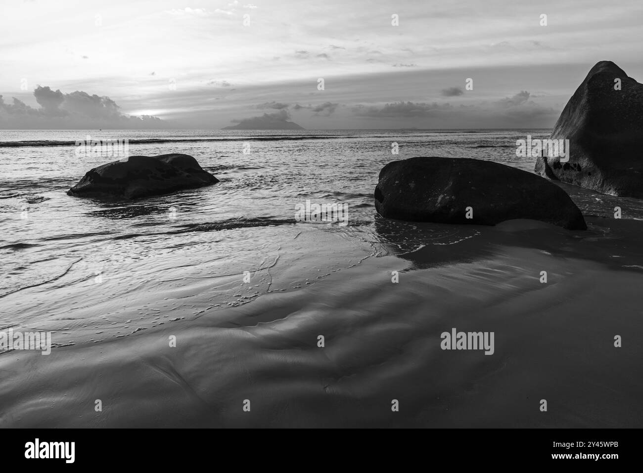 Photographie de paysage noir et blanc avec sable humide et silhouettes de rochers côtiers sur le coucher du soleil. Plage de beau Vallon, île de Mahé, Seychelles Banque D'Images