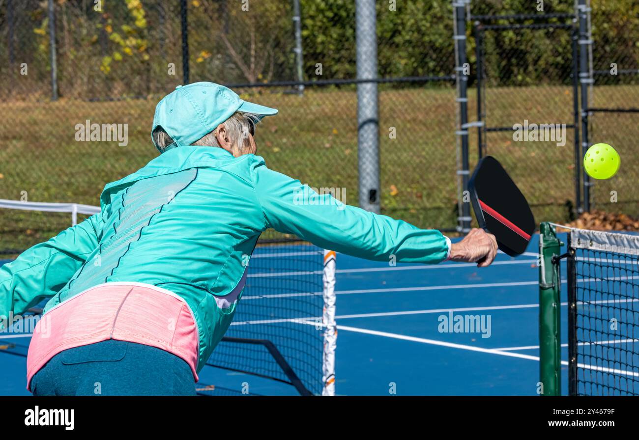 Femme senior s'étire pour une courte volée pendant le jeu de pickleball Banque D'Images