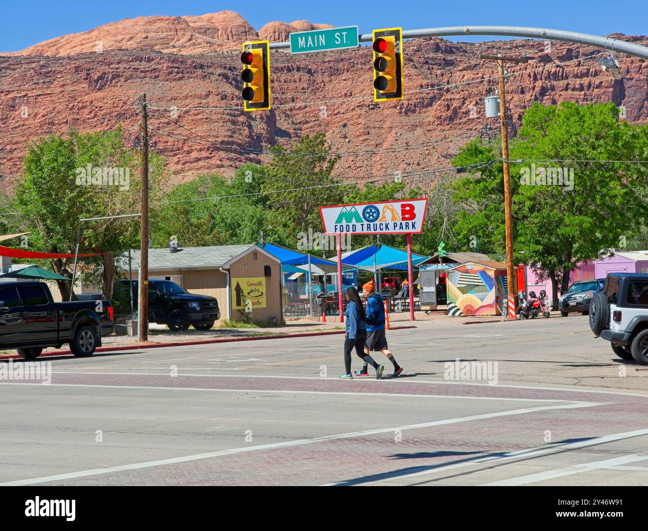 Piétons traversant la rue au parc des camions alimentaires de Moab avec un fond rouge de falaises de bord de Moab — Moab Utah, avril 2024 Banque D'Images