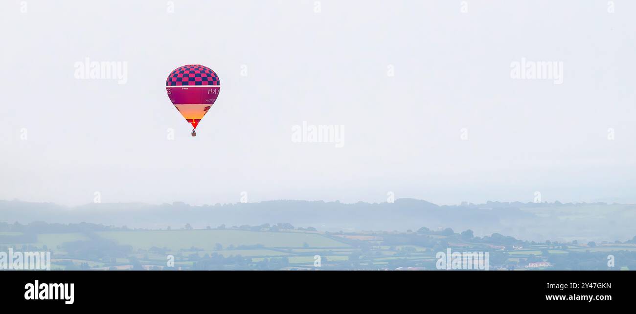 Ballon rouge volant haut au-dessus des niveaux Somerset avec brûleur allumé très tôt le matin sur une journée très brumeuse et terne, Royaume-Uni Banque D'Images