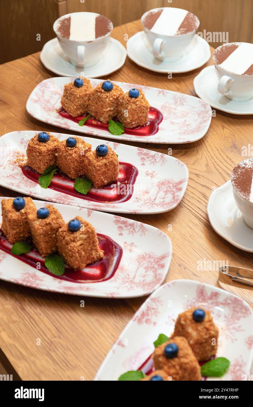 Portions de gâteau Millefeuille à base de pâte feuilletée sur assiettes et cappuccino dans des tasses blanches sur une table dans un restaurant. Dessert français, gâteau Napoléon. Banque D'Images