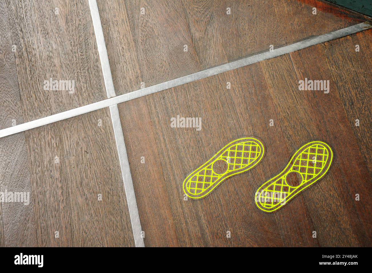 Gros plan d'un plancher en bois avec des empreintes de chaussures jaunes et des lignes argentées croisées Banque D'Images