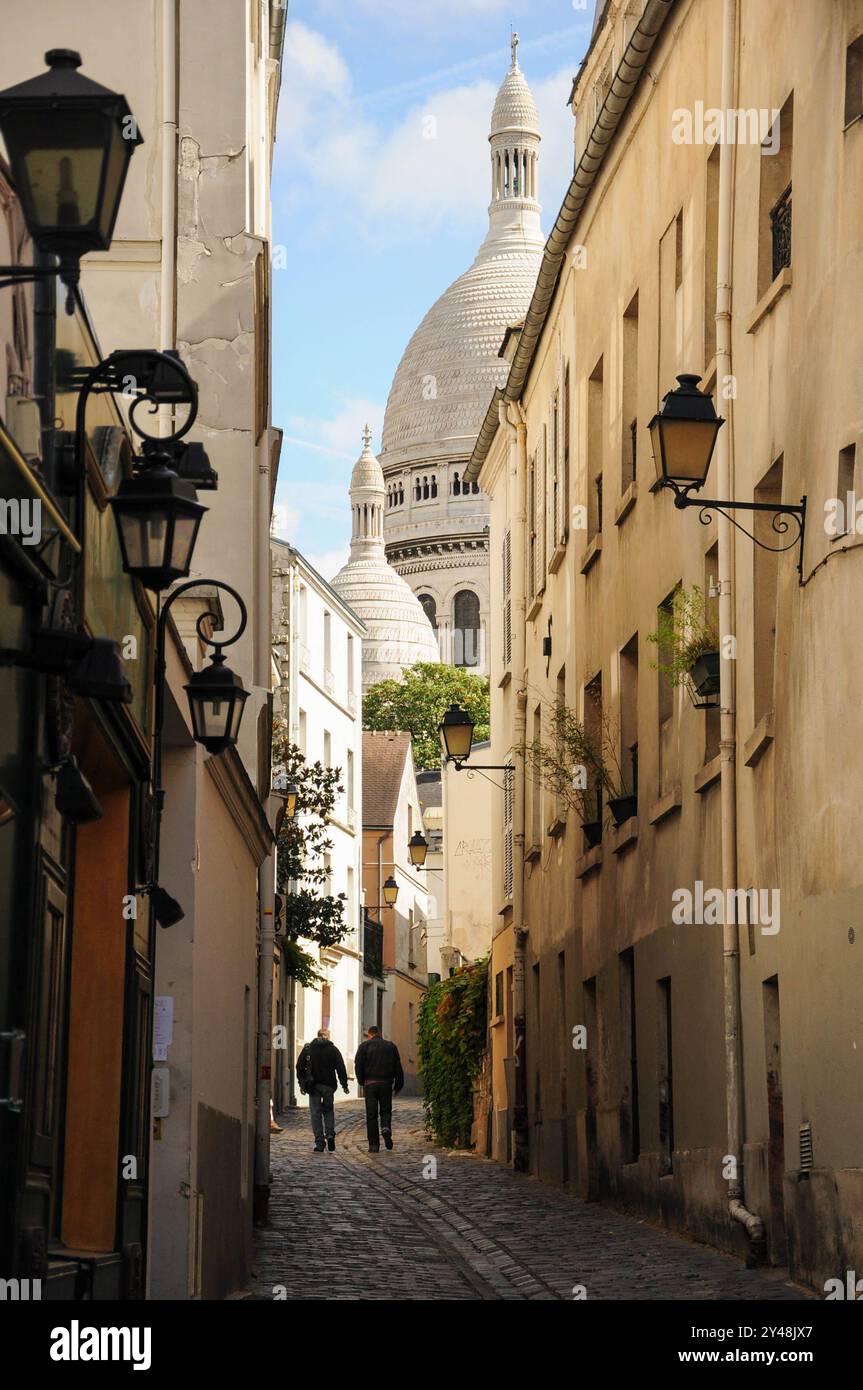 Paris, Ille de France, France. 16 septembre 2024 : deux hommes marchant dans une rue étroite de Paris avec la basilique du Sacré-cœur en arrière-plan. Banque D'Images