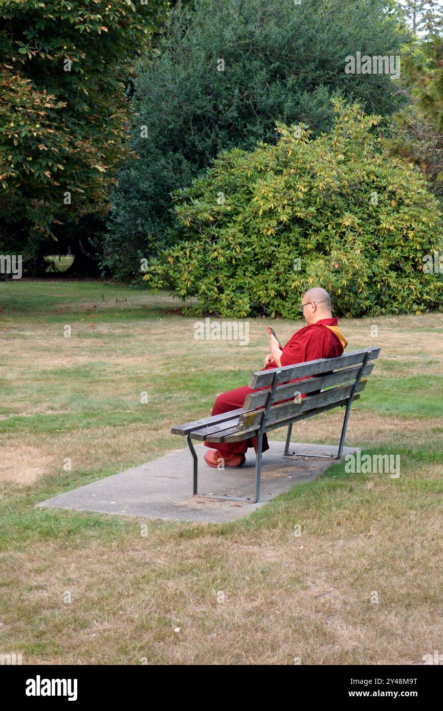 Moine bouddhiste assis sur un banc de parc regardant comme son téléphone cellulaire, Vancouver, BC, Canada Banque D'Images