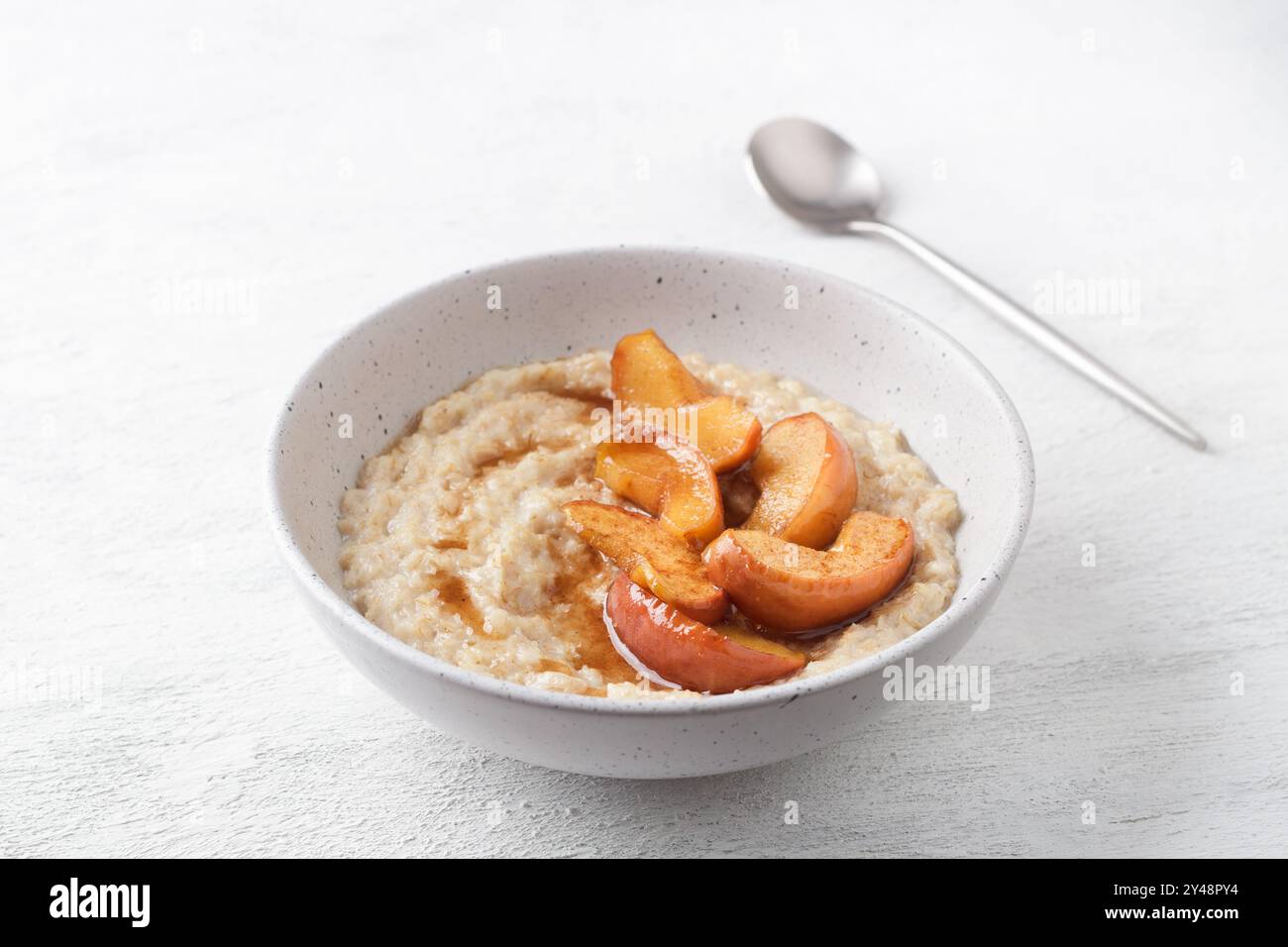 Bouillie d'avoine sucrée avec tranches de pomme cuites au four, cannelle et sauce caramel dans un bol gris sur un fond clair, vue de dessus. Délicieuse cuisine maison Banque D'Images