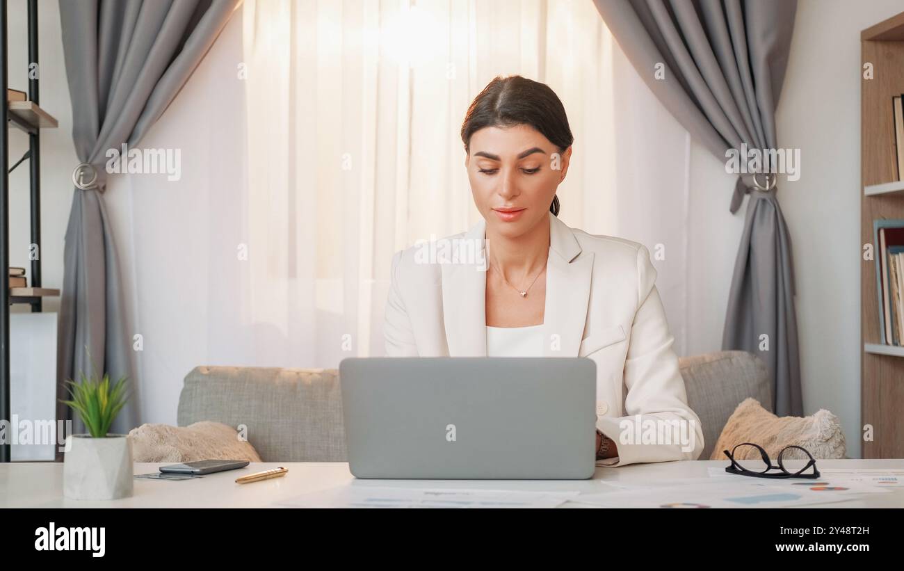 Chef de bureau. Femme qui travaille. Projet numérique. Inspiré dame élégante dame tapant ordinateur portable assis dans l'intérieur de la pièce de bureau léger. Banque D'Images