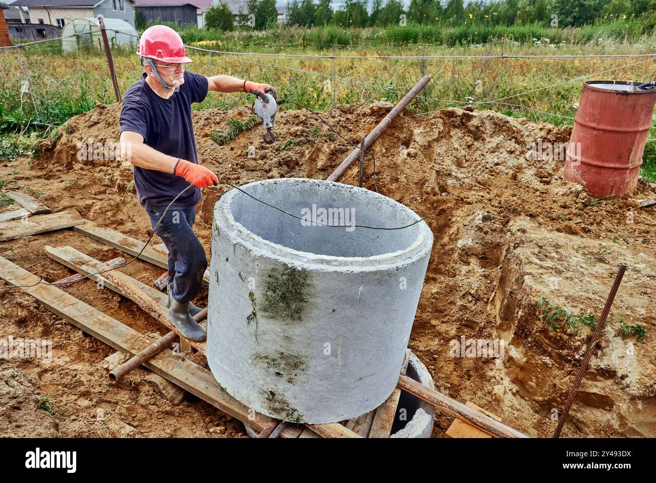 Le gréeur a poussé un anneau de béton sur un autre pendant la construction de la fosse septique à l'aide de rouleaux et de treuil. Banque D'Images