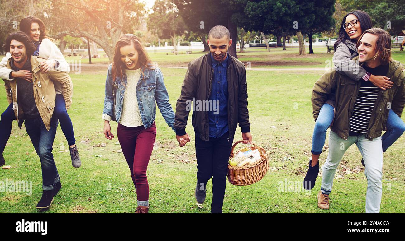Des gens heureux, des amis et se tenant la main avec un panier de pique-nique au parc pour se lier ou se réunir dans la nature. Couples, hommes et femmes avec sourire dedans Banque D'Images