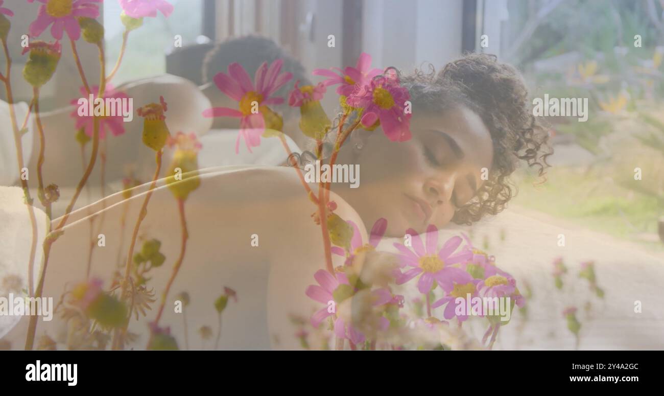 Image de fleurs roses dans le jardin sur la femme biraciale couchée sur la table de massage Banque D'Images