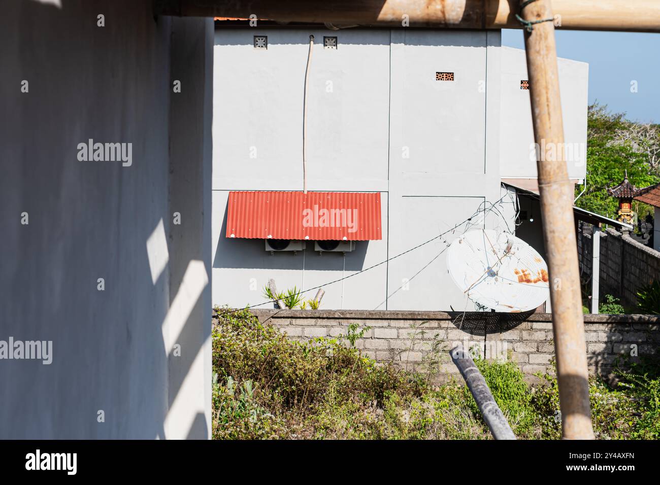 Une vue d'un boolding blanc avec un toit rouge et antenne parabolique, entouré de verdure. L'image capture un chantier de construction avec un échafaudage en bambou Banque D'Images
