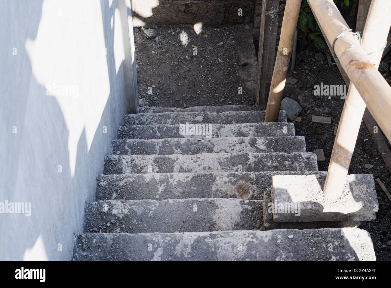 Un ensemble d'escaliers en béton menant vers le bas, partiellement recouverts de poussière et de saleté. Les escaliers sont flanqués d'une balustrade en bambou d'un côté, et le surrou Banque D'Images