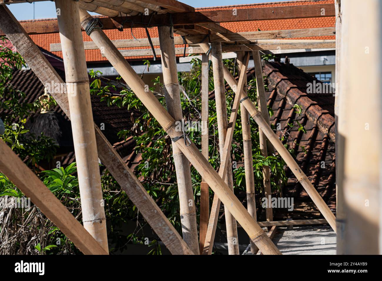 Une vue rapprochée d'une structure d'échafaudage en bambou sur fond de toits en tuiles traditionnels. La lumière du soleil projette des ombres sur le bambou, highlightin Banque D'Images
