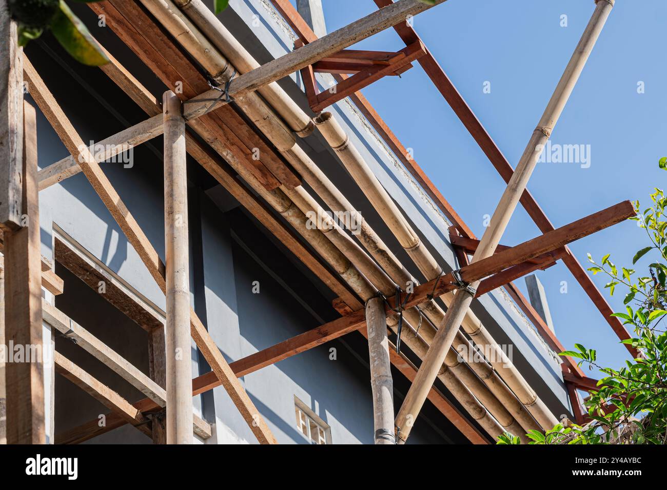 Une vue rapprochée d'une structure d'échafaudage en bambou sur fond de toits en tuiles traditionnels. La lumière du soleil projette des ombres sur le bambou, highlightin Banque D'Images