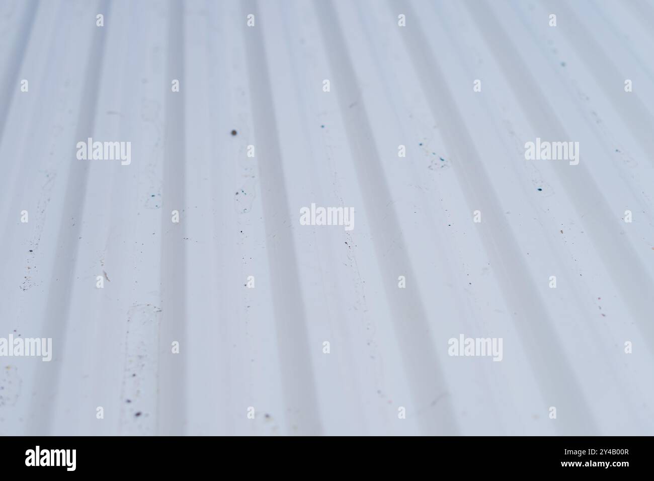 Gros plan d'une surface blanche texturée avec des rainures parallèles, montrant des particules de saleté et de poussière. La surface semble être en plastique ou en métal Banque D'Images