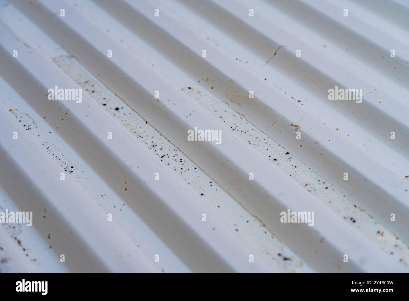 Gros plan d'une surface blanche texturée avec des rainures parallèles, montrant des particules de saleté et de poussière. La surface semble être en plastique ou en métal Banque D'Images