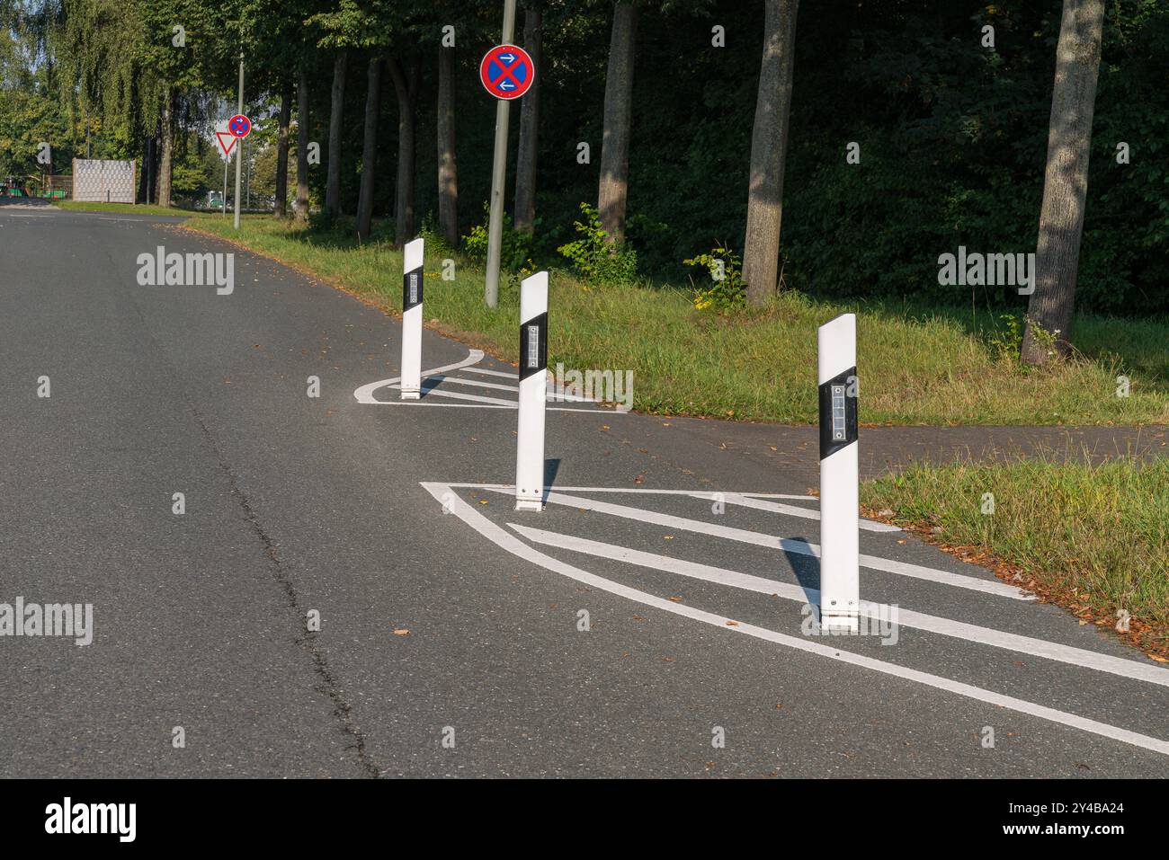 Des poteaux de circulation bordent une route courbe, guidant les véhicules vers le virage. La région présente une végétation luxuriante, offrant une toile de fond naturelle au cadre urbain Banque D'Images