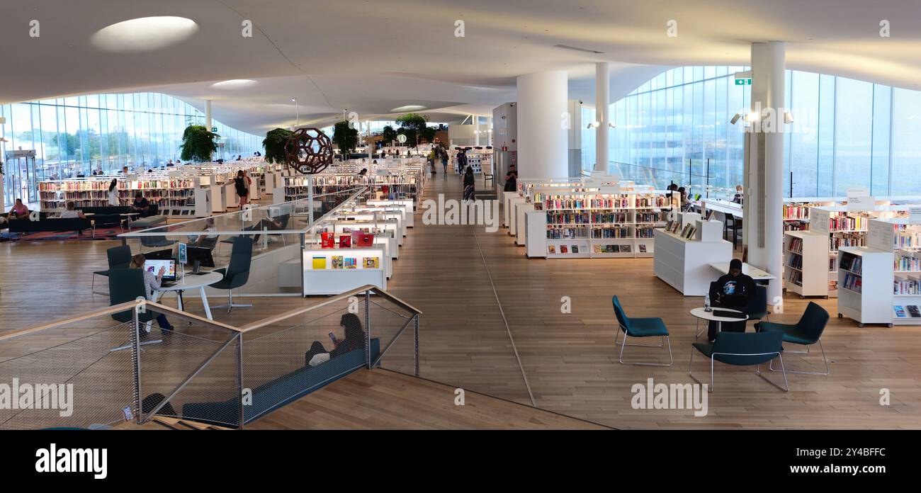 Helsinki, Finlande, le 18 juillet 2024 : L'intérieur moderne de la bibliothèque est baigné de lumière naturelle et les gens naviguent ou lisent par un après-midi calme. Bibliothèque Oodi Banque D'Images