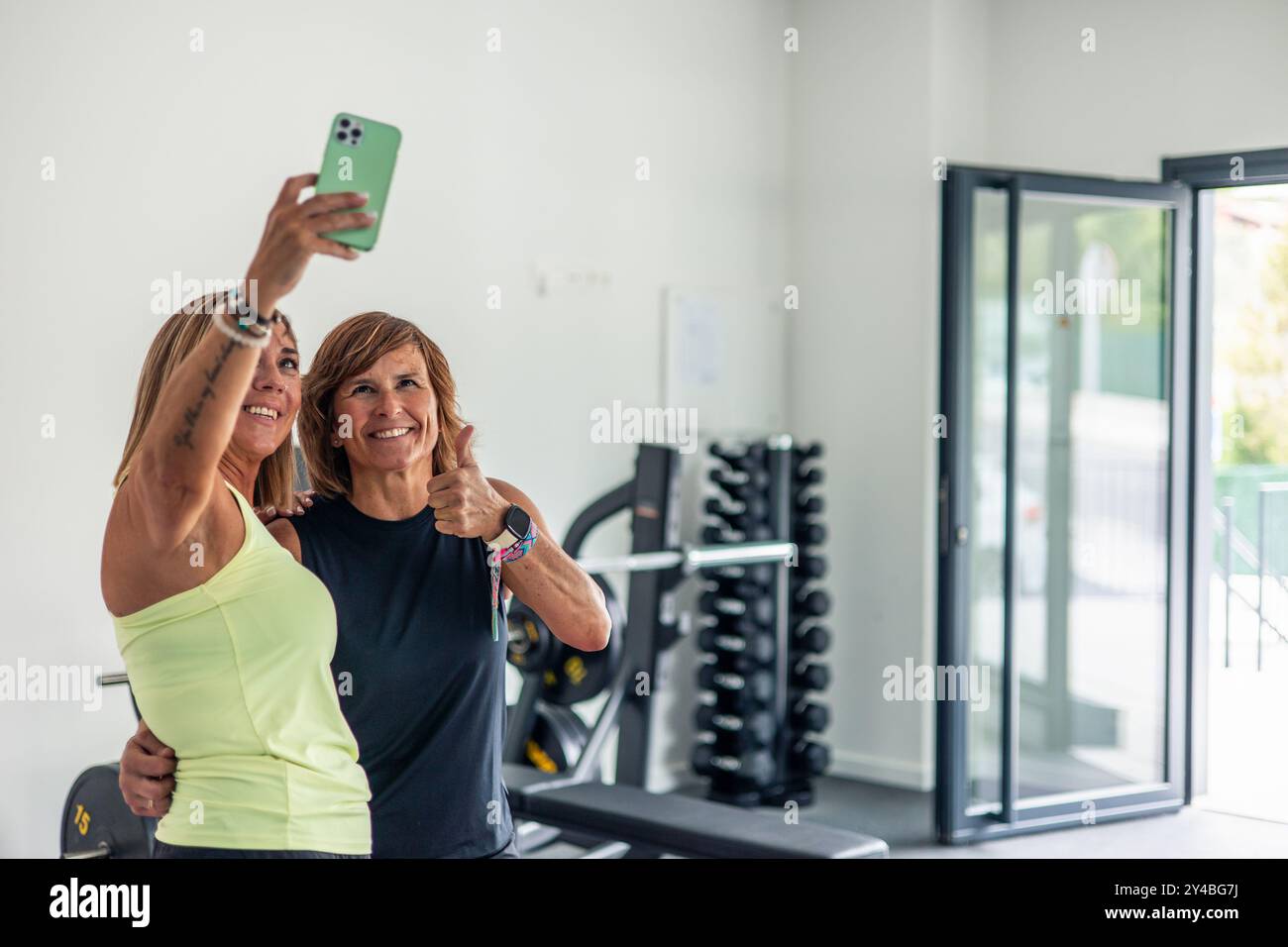 Copyspace deux femmes matures en tenue sportive, souriantes et pleines d'énergie, prennent un selfie avec smartphone à la salle de gym après une séance d'entraînement intense. Th Banque D'Images