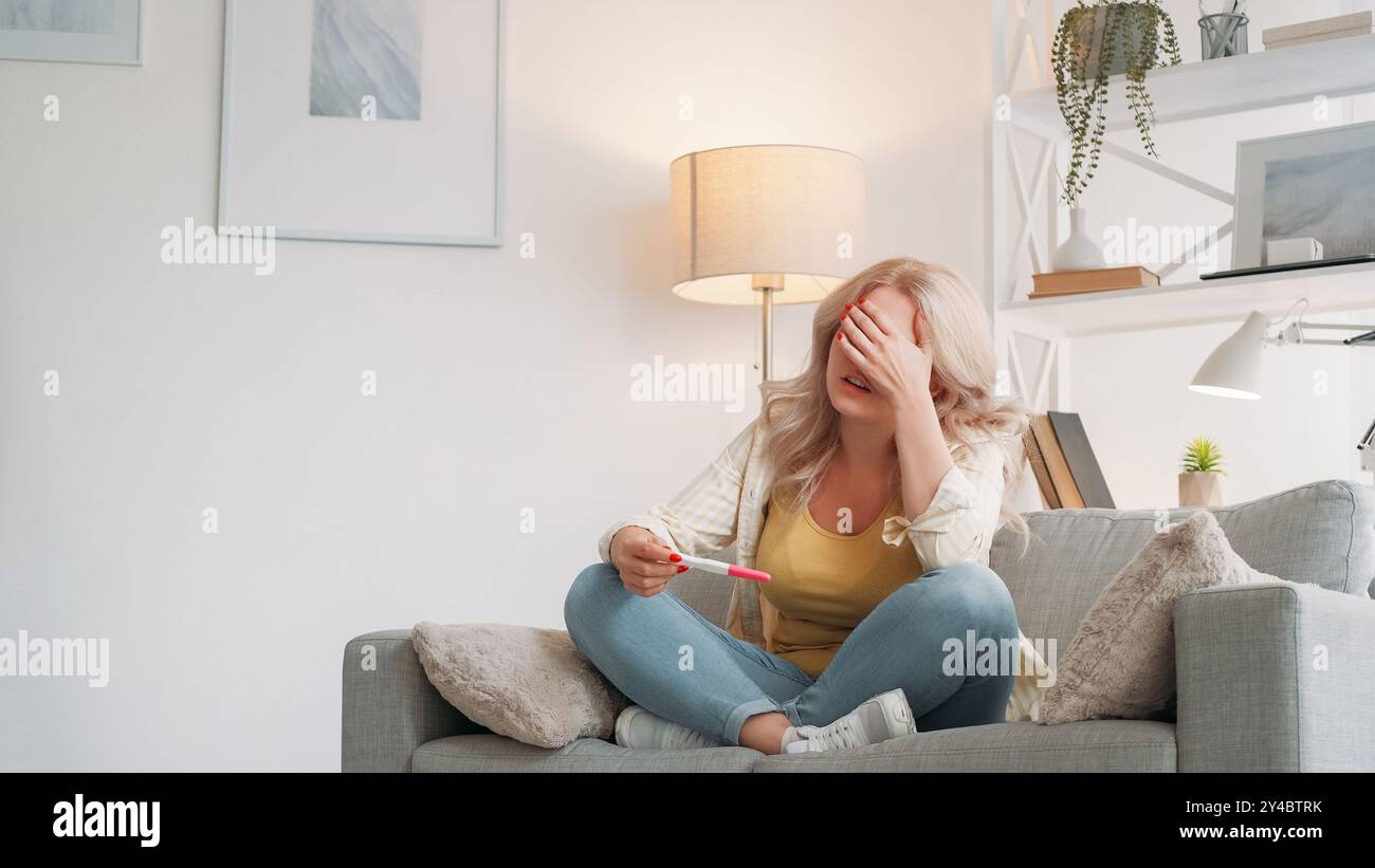 L'espérance de grossesse. Femme désespérée. Mauvaise nouvelle. Dame pleurer bouleversée obtenant un résultat de test négatif ressentant du chagrin assis canapé lumière intérieur de la pièce. Banque D'Images