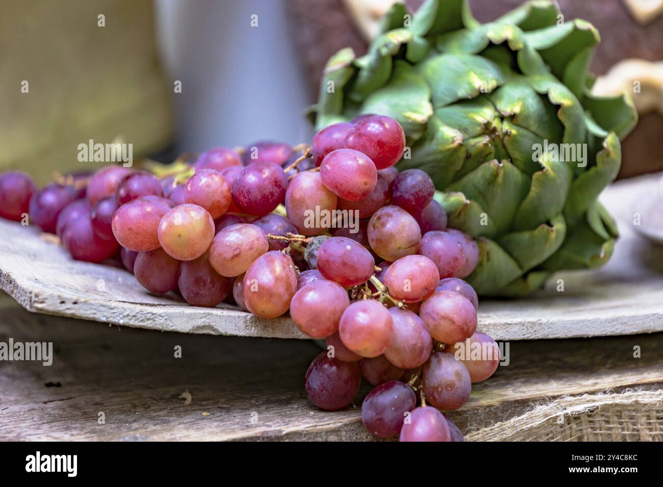 Étal de marché avec raisins rouges et artichauts sur une planche de bois rustique Banque D'Images