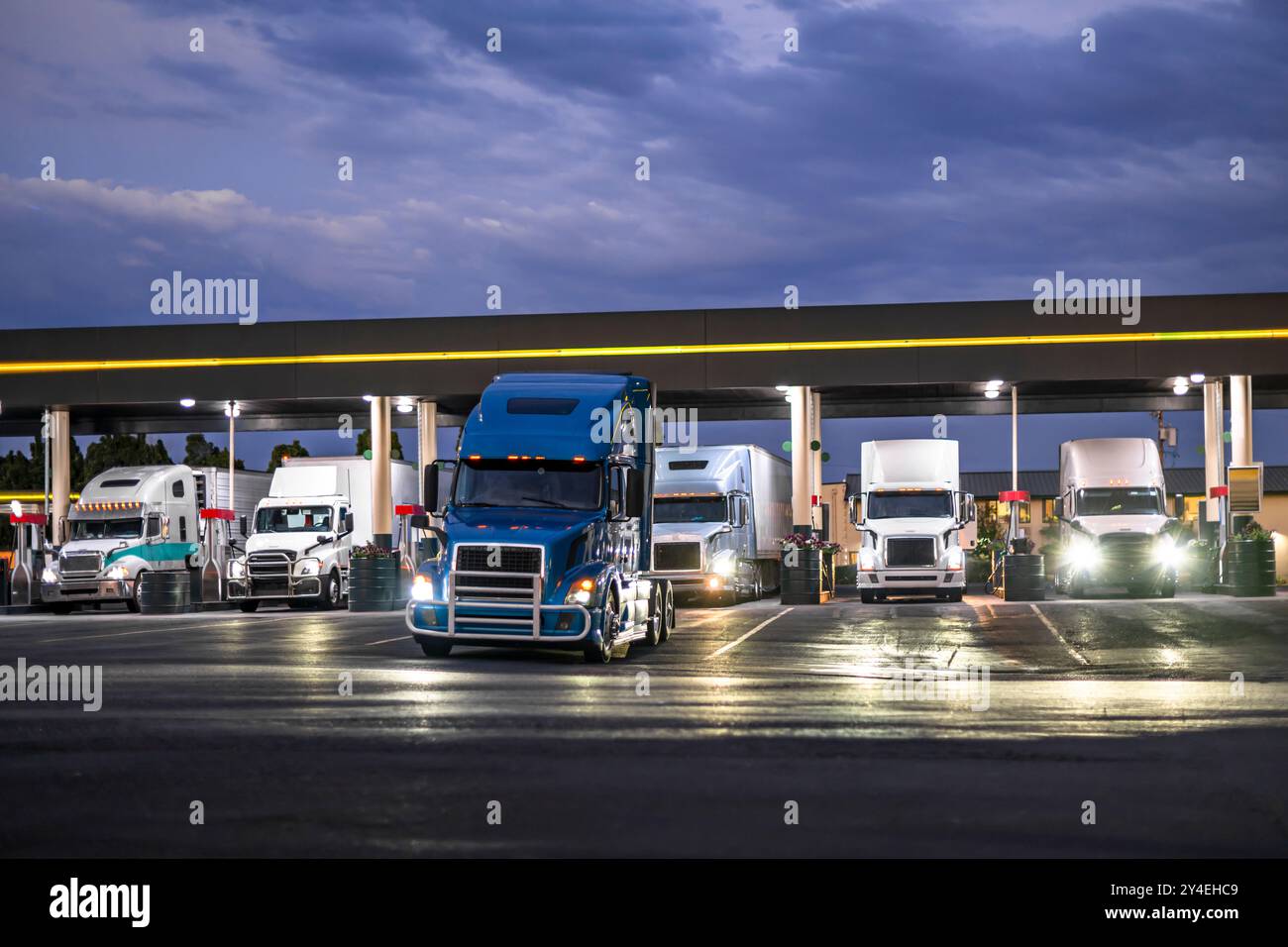 Transporteurs de long-courrier industriels les semi-remorques de gros engins commerciaux avec semi-remorques remplissent leurs réservoirs de carburant à la station-service d'arrêt de camions la nuit à Banque D'Images