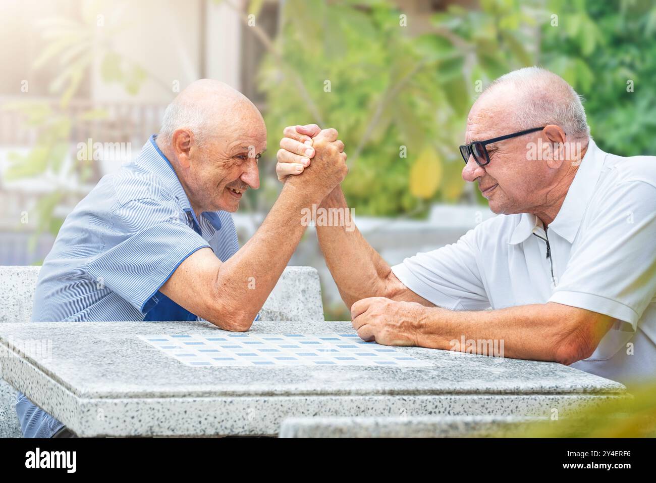 Des amis seniors s'affrontent dans le bras de fer à une table à l'extérieur Banque D'Images