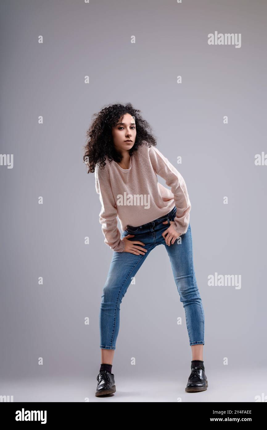 La mannequin aux cheveux bouclés pose avec ses mains sur ses hanches, ses jambes écartées et ses genoux légèrement pliés, penchés en avant Banque D'Images
