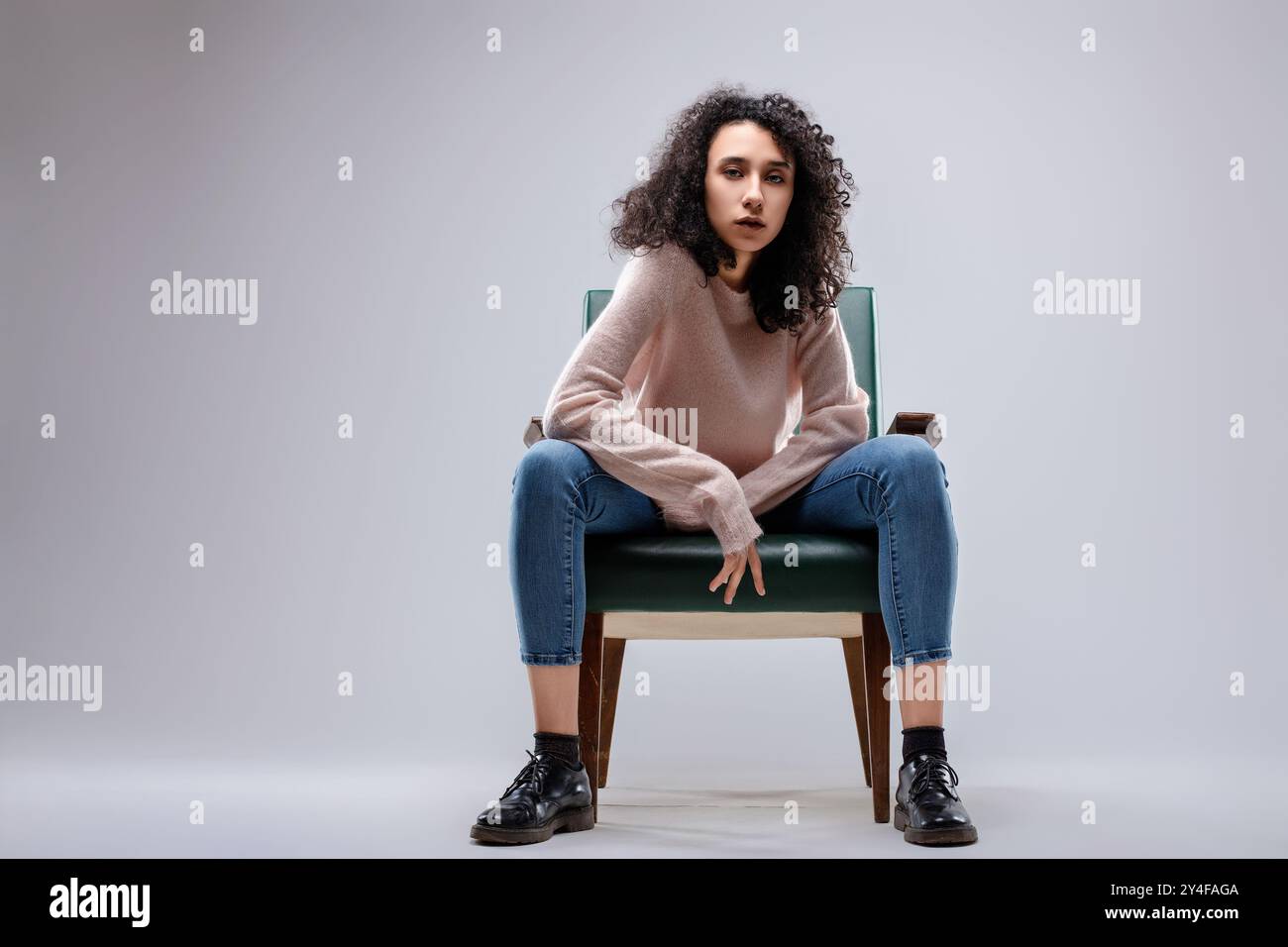 Mannequin avec les cheveux bouclés pose assise sur un fauteuil vintage avec ses jambes écartées et les bras reposant sur ses cuisses Banque D'Images