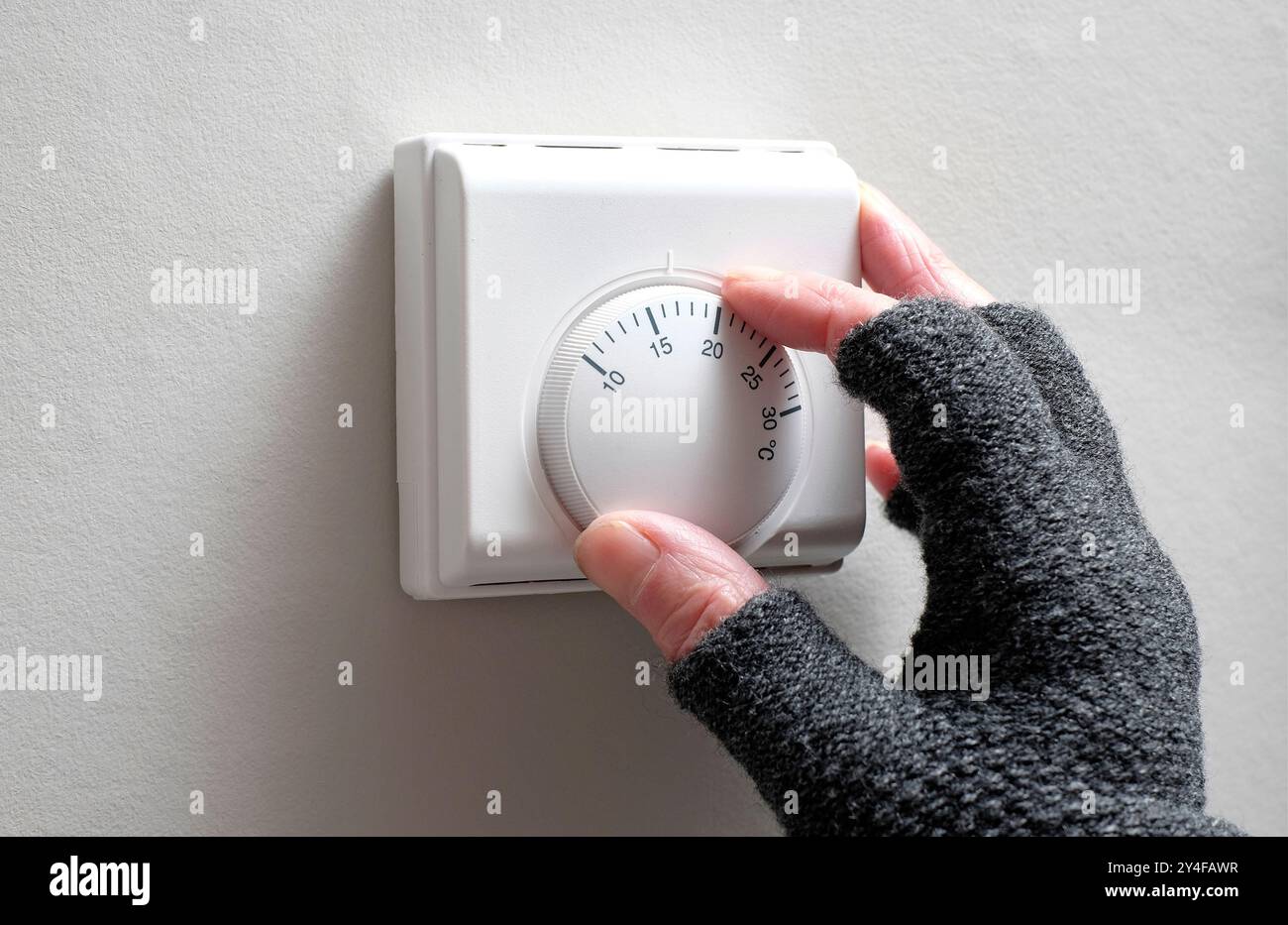 personne senior tournant le thermostat de pièce vers le bas pour économiser de l'argent Banque D'Images