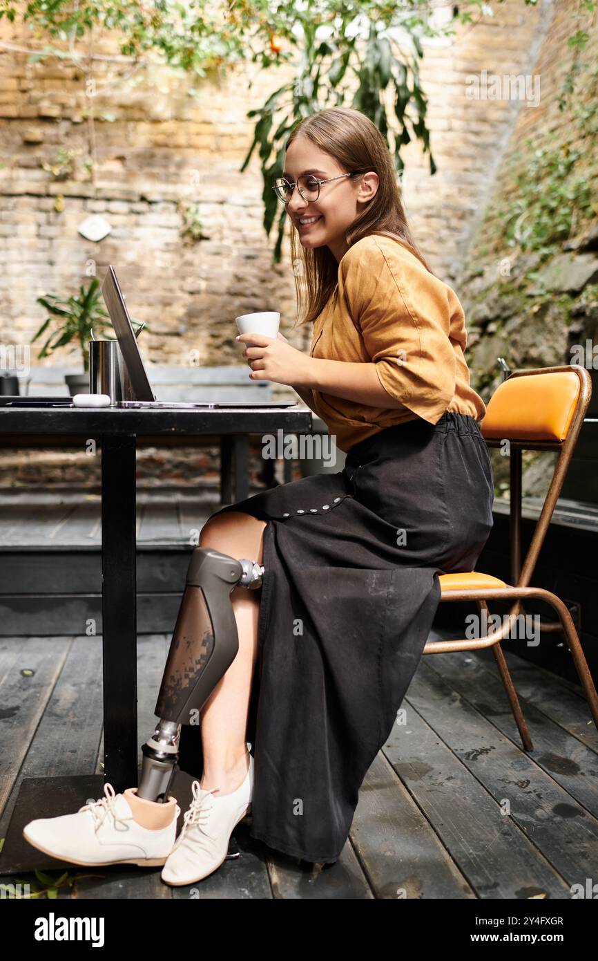 Dans un charmant café, une jeune femme avec un membre artificiel savoure le café et s'engage avec son ordinateur portable, embrassant la vie quotidienne. Banque D'Images