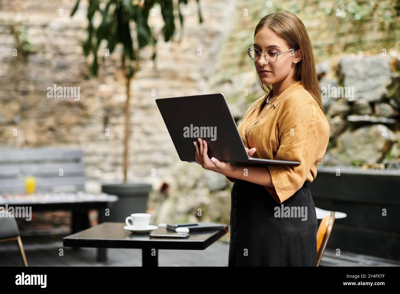 Une jeune femme embrasse sa vie quotidienne, gérant habilement son ordinateur portable dans un cadre de café confortable. Banque D'Images