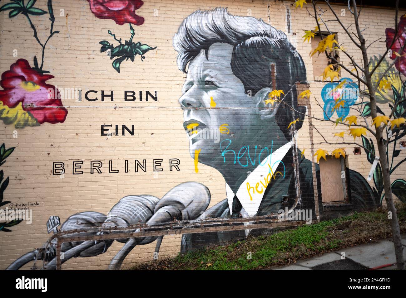 John F Kennedy Ich Bin Ein Berliner Mural Washington DC // WASHINGTON DC — Une murale distinctive orne l'extérieur du café Ich Bin Ein Berliner dans le quartier historique de Georgetown à Washington DC. L'œuvre représente le président John F. Kennedy en noir et blanc devant un microphone prononçant son célèbre discours, entouré de fleurs vibrantes et colorées qui contrastent avec la représentation monochromatique du président. La fresque commémore l'emblématique adresse de Kennedy « Ich bin ein Berliner » de 1963 à Berlin-Ouest pendant la guerre froide. Georgetown, situé le long de la rivière Potomac, est connu pour Banque D'Images