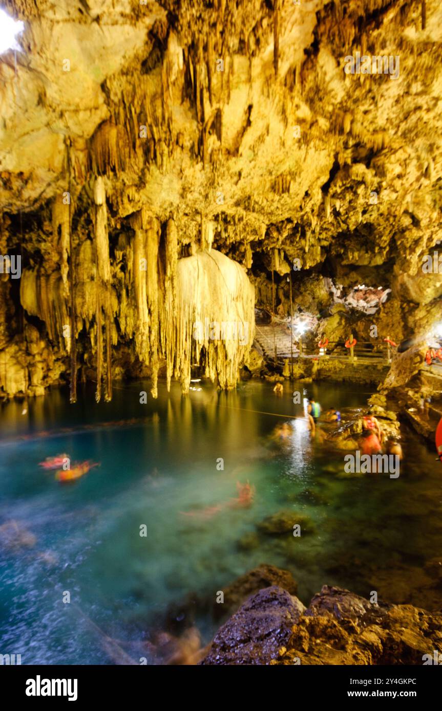 VALLADOLID, Mexique — les nageurs apprécient les eaux cristallines du Cenote X'kakah près de Valladolid, Mexique. Ce trou de baignade souterrain, qui fait partie du vaste réseau de voies navigables souterraines du Yucatan, présente une petite ouverture dans le plafond qui permet à la lumière et à l'air frais d'entrer, ainsi que des stalactites impressionnantes. La température constante de l'eau de 24 °C (76 °F) en fait une attraction populaire toute l'année. Banque D'Images