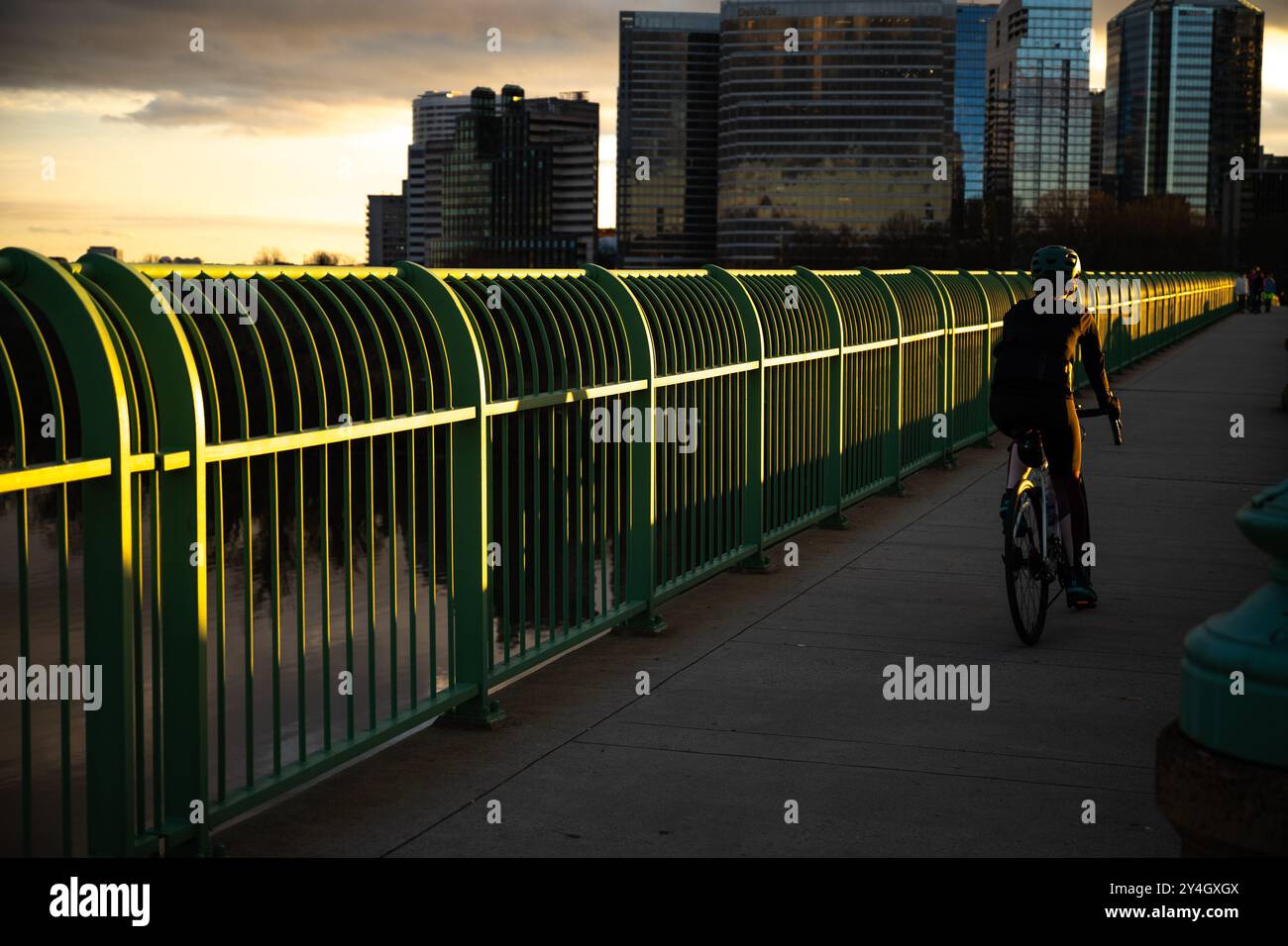 Cycliste de Key Bridge Rosslyn Skyline Washington DC // WASHINGTON DC — Un cycliste traverse Key Bridge, attrapant les derniers rayons de soleil avant le coucher du soleil alors qu'il voyage entre Georgetown et Rosslyn. Les immeubles de bureaux de Rosslyn créent une toile de fond distinctive derrière le cycliste sur cette traversée historique du fleuve Potomac. Le pont Francis Scott Key sert de lien de transport important reliant Washington DC à Arlington, en Virginie. Le pont accueille divers navetteurs, y compris les cyclistes voyageant entre les deux centres urbains. Banque D'Images