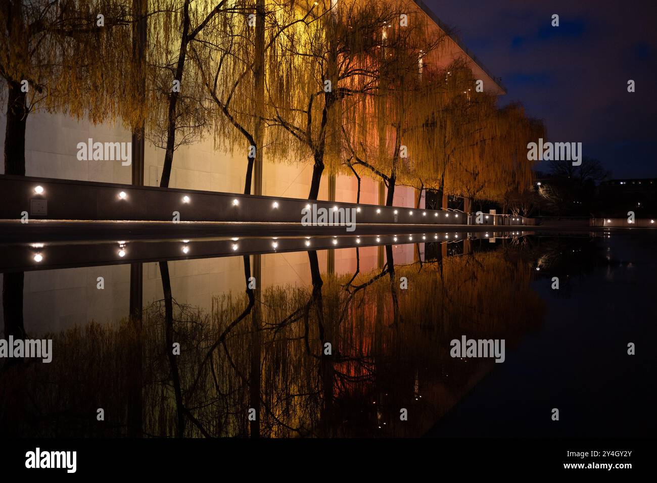 Kennedy Center illuminé la nuit Washington DC // WASHINGTON DC — le John F. Kennedy Center for the Performing Arts est illuminé la nuit avec des lumières colorées pour le Kennedy Center Honors, son reflet capturé dans une flaque après une pluie récente. Le monument culturel emblématique sur le fleuve Potomac met en valeur sa beauté architecturale et son importance en tant que lieu national pour les art. Banque D'Images