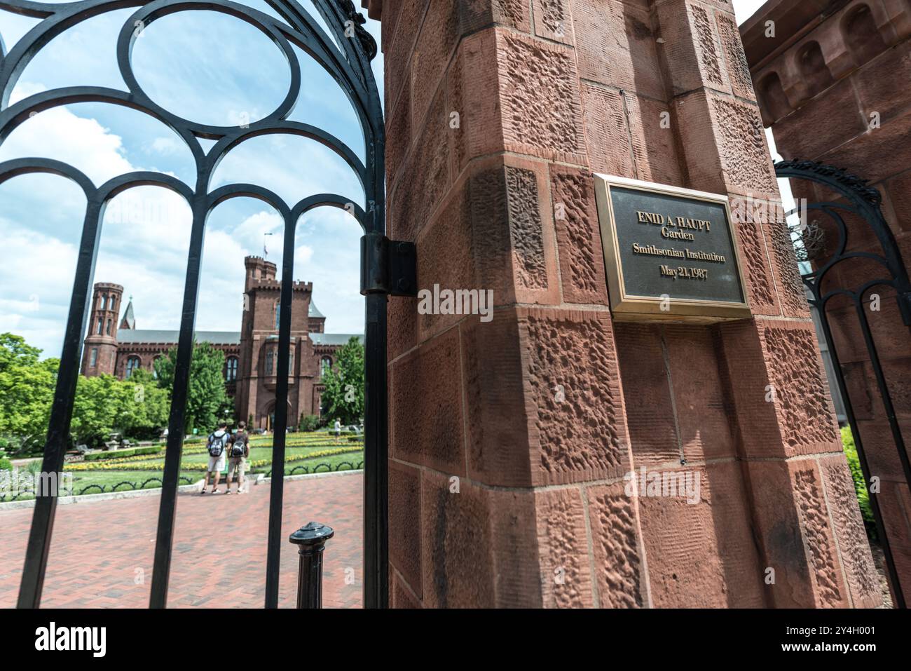 Enid A Haupt Garden Smithsonian Castle Washington DC | WASHINGTON D.C., États-Unis — Une plaque de bronze sur les portes Renwick marque l'entrée officielle du jardin Enid A. Haupt, encadrant une vue en fer forgé du château Smithsonian au-delà. Fabriquées vers 1979 à partir d'un croquis de 1849 par l'architecte du château James Renwick Jr., les portes s'ouvrent sur le jardin de 4,2 acres dédié le 21 mai 1987. Banque D'Images