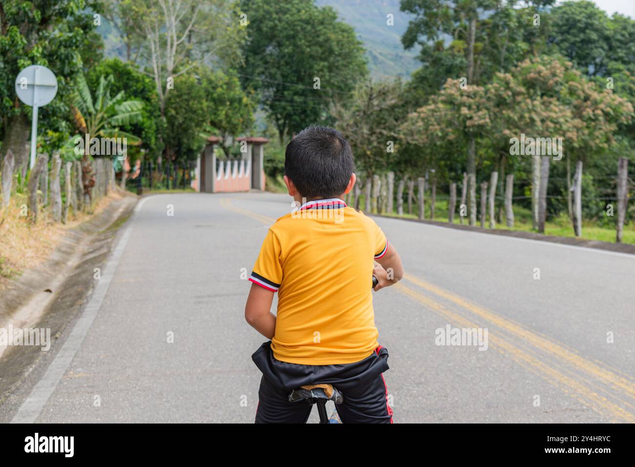 Portrait d'un enfant qui monte une vieille bicyclette sur une route en Colombie, vu de derrière Banque D'Images