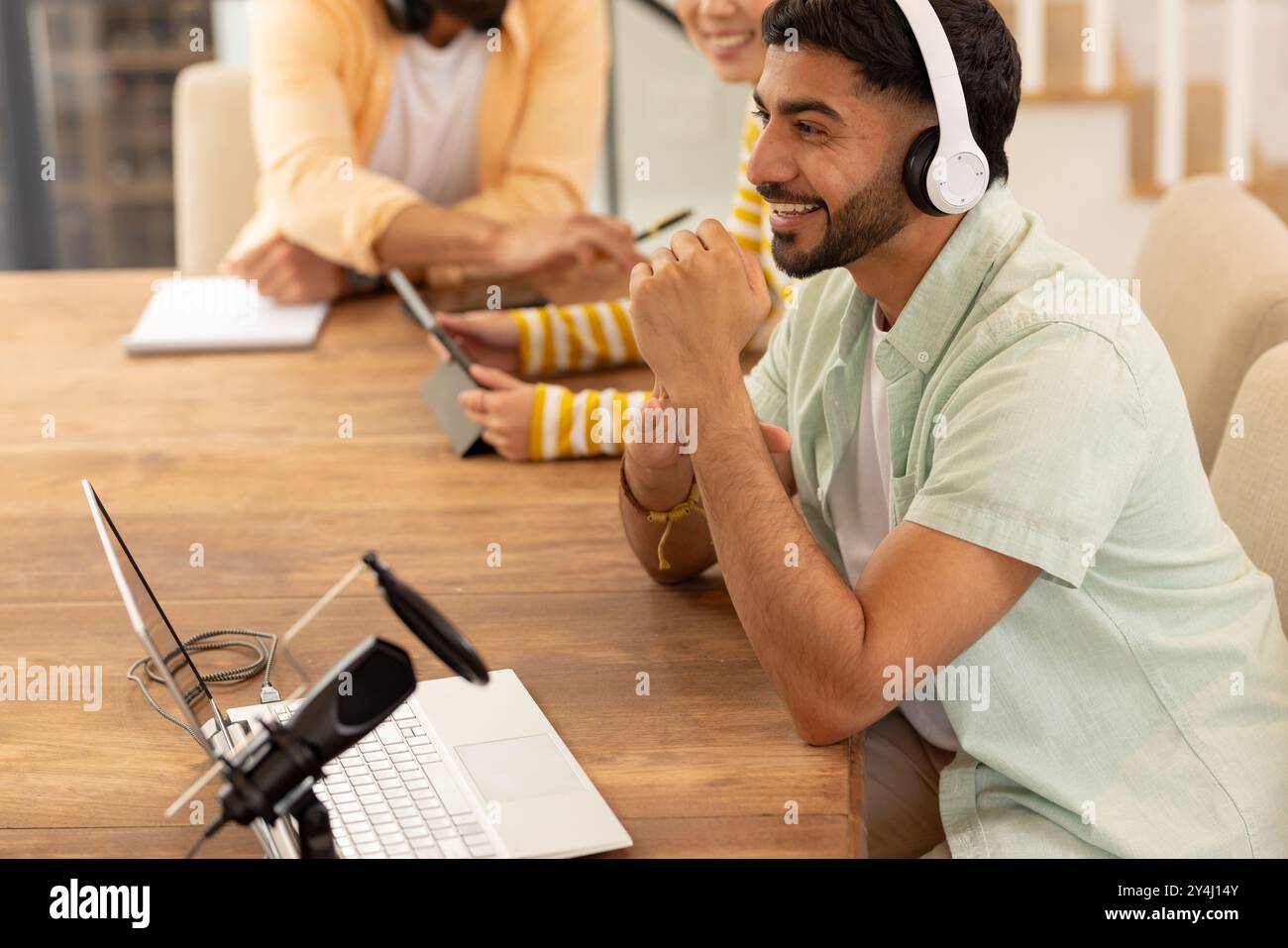 En utilisant un ordinateur portable et en portant des écouteurs, homme souriant tout en travaillant avec des amis Banque D'Images