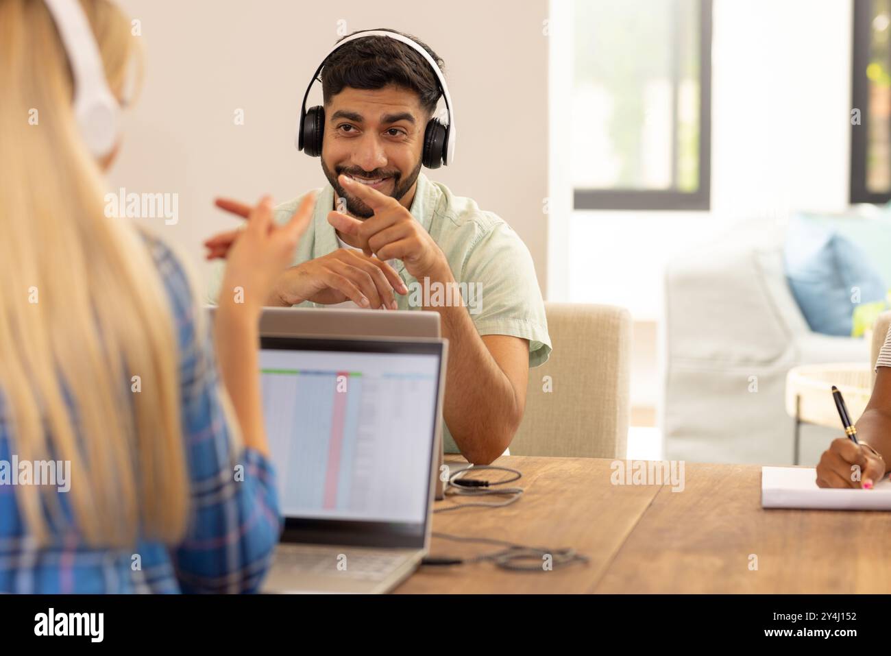 En utilisant un ordinateur portable et en portant des écouteurs, homme souriant et parlant avec des amis Banque D'Images