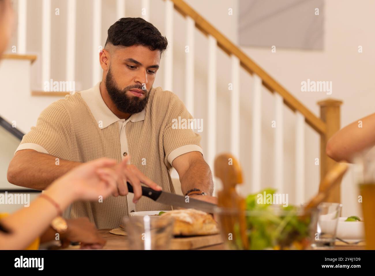 Couper le pain, l'homme préparant le repas avec divers amis à la table à manger à la maison Banque D'Images