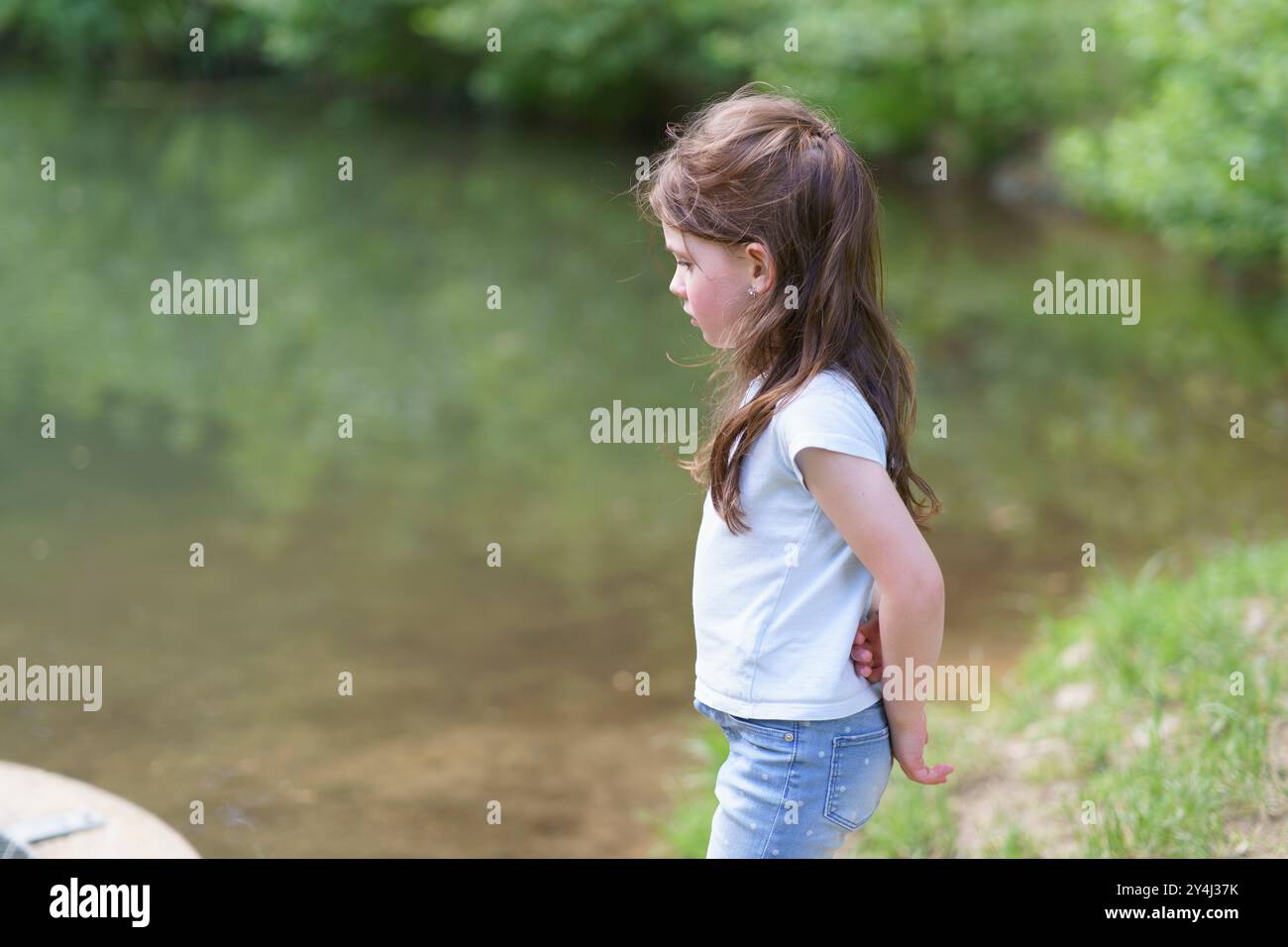 Petite fille préscolaire mignonne dans un T-shirt joue sur le fond d'un étang. Concept d'enfance heureuse en plein air Banque D'Images