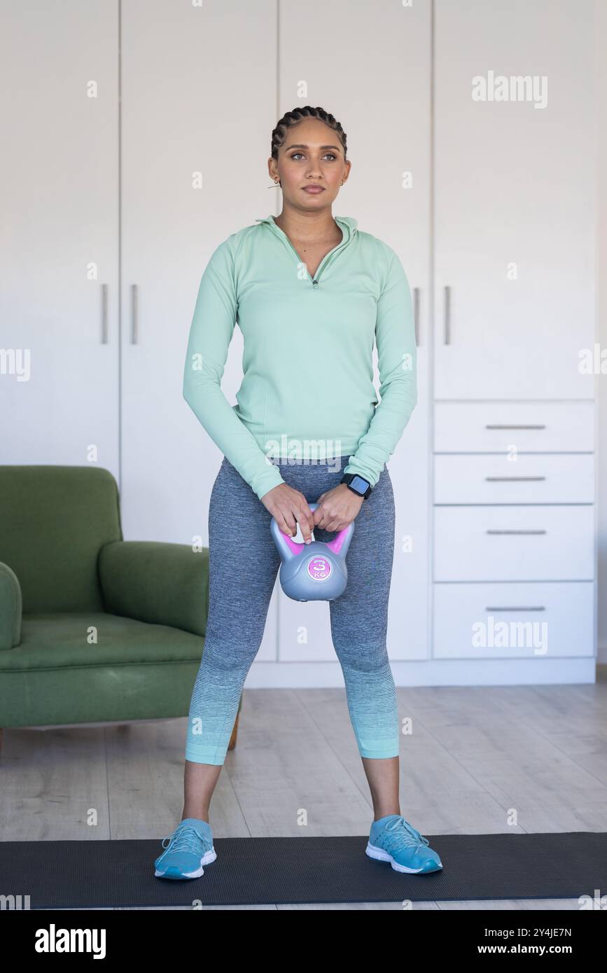 Tenant kettlebell, femme exerçant à la maison dans des vêtements d'entraînement confortables Banque D'Images