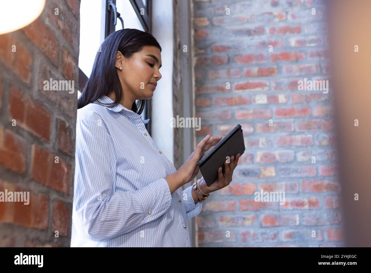 En utilisant la tablette, femme d'affaires travaillant dans un bureau moderne avec des murs de briques apparentes Banque D'Images