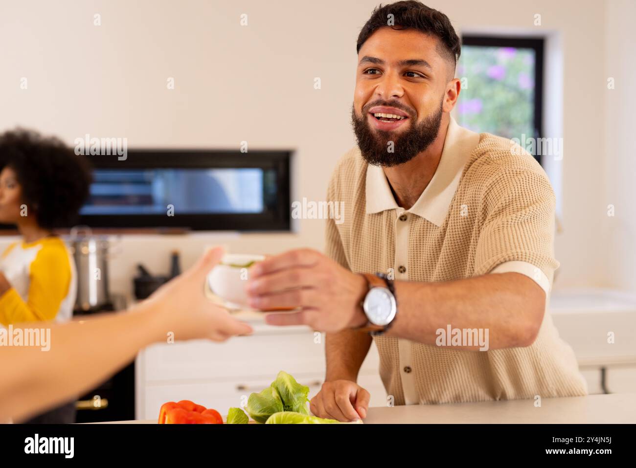 Homme souriant dans la cuisine remettant la tasse à un ami tout en préparant les légumes Banque D'Images