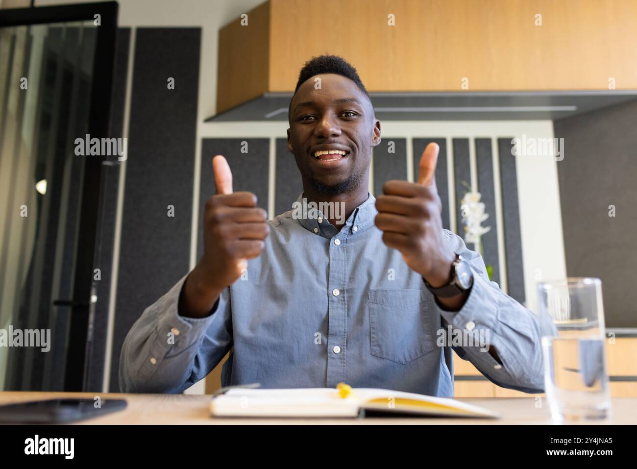 Homme souriant donnant les pouces dans le bureau, assis au bureau avec un ordinateur portable Banque D'Images