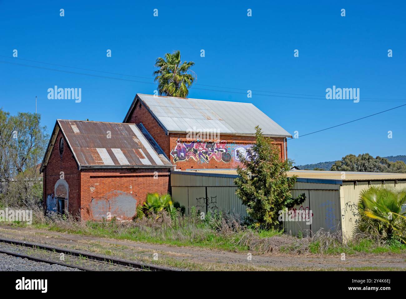 Bâtiments en briques abandonnés avec toits à pignon et graffitis et une végétation envahie. Banque D'Images